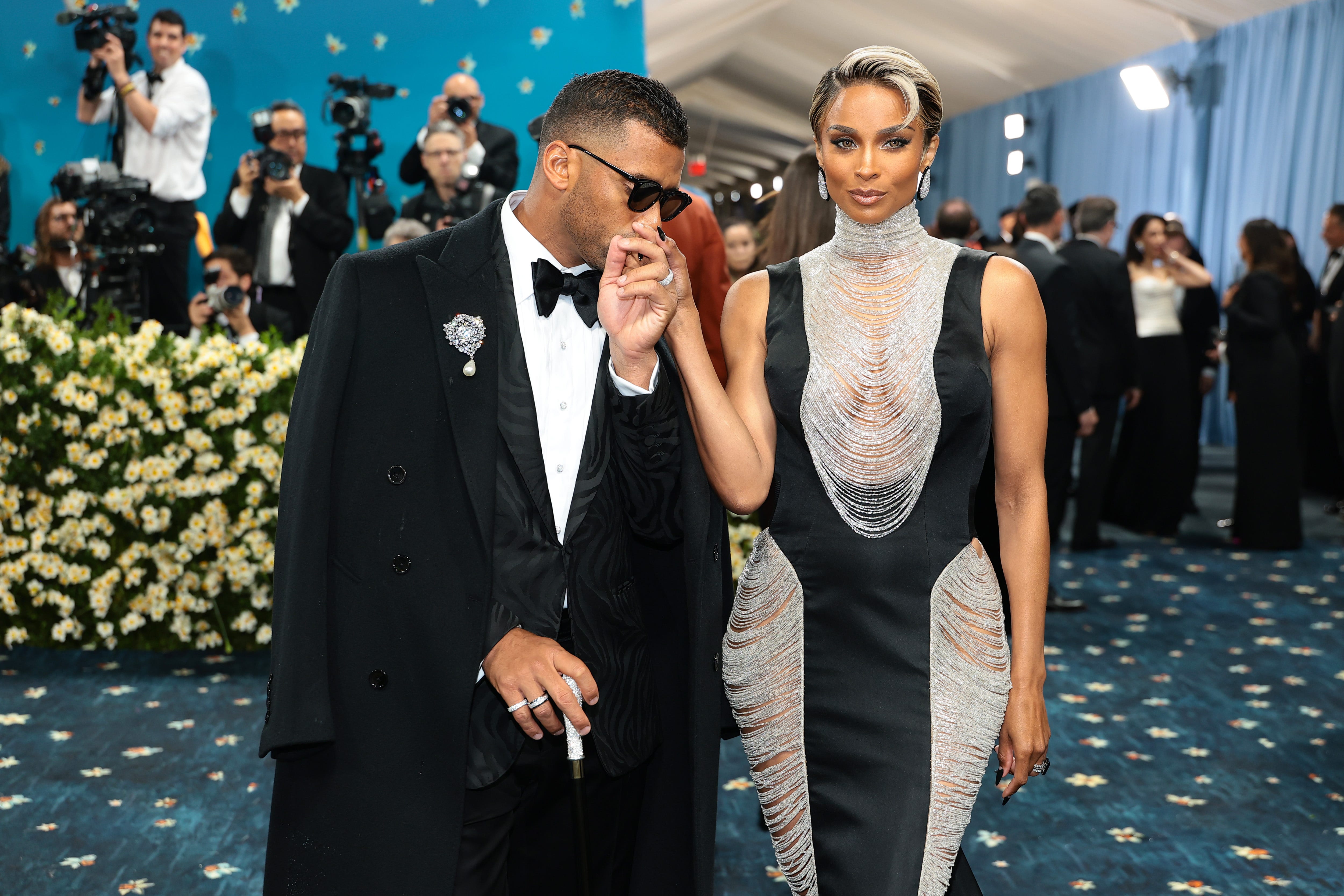 Russell Wilson in a tuxedo and cape and Ciara in a beaded gown at the 2025 Met Gala.