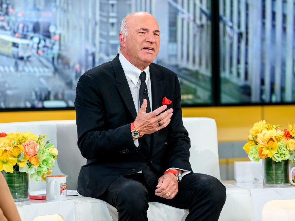 Kevin O'Leary sitting on a couch in a studio during an interview.