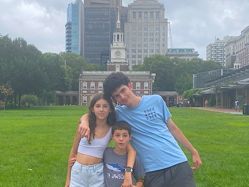 Three of the author's kids on a lawn in front of buildings in a city.