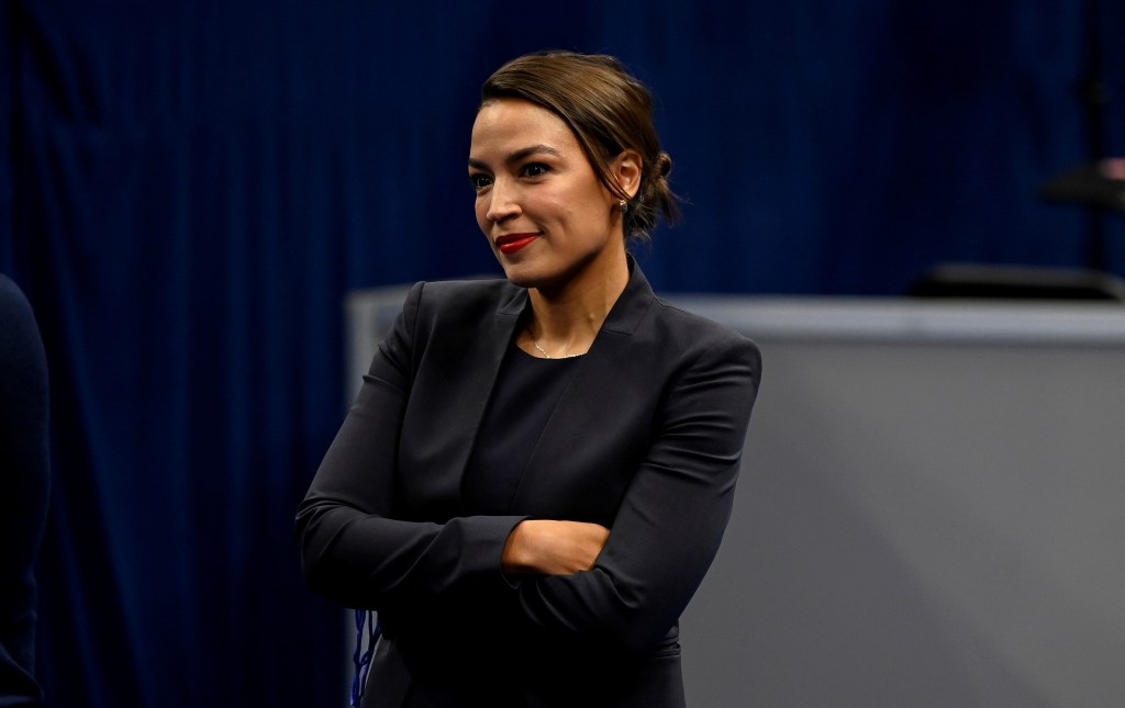 Alexandria Ocasio-Cortez wearing a dark suit, smiling, and looking to her right.