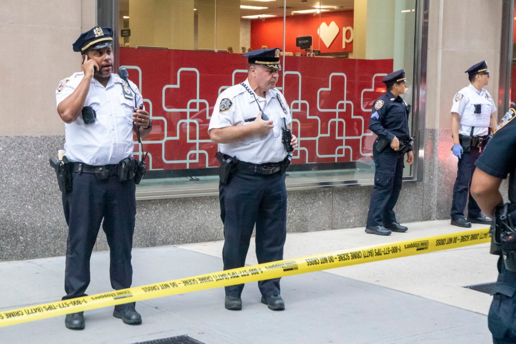 NYPD officers at the scene of a shooting in Midtown Manhattan behind yellow crime scene tape.