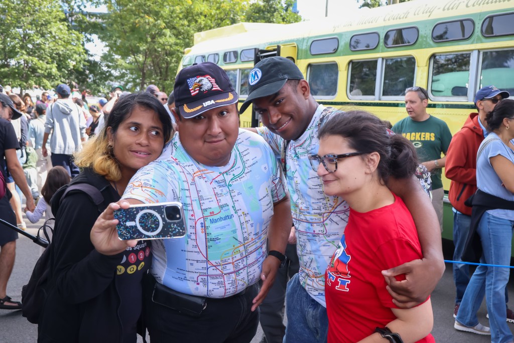 Four people posing for a photo in front of a yellow bus at the 2025 Bus Festival.