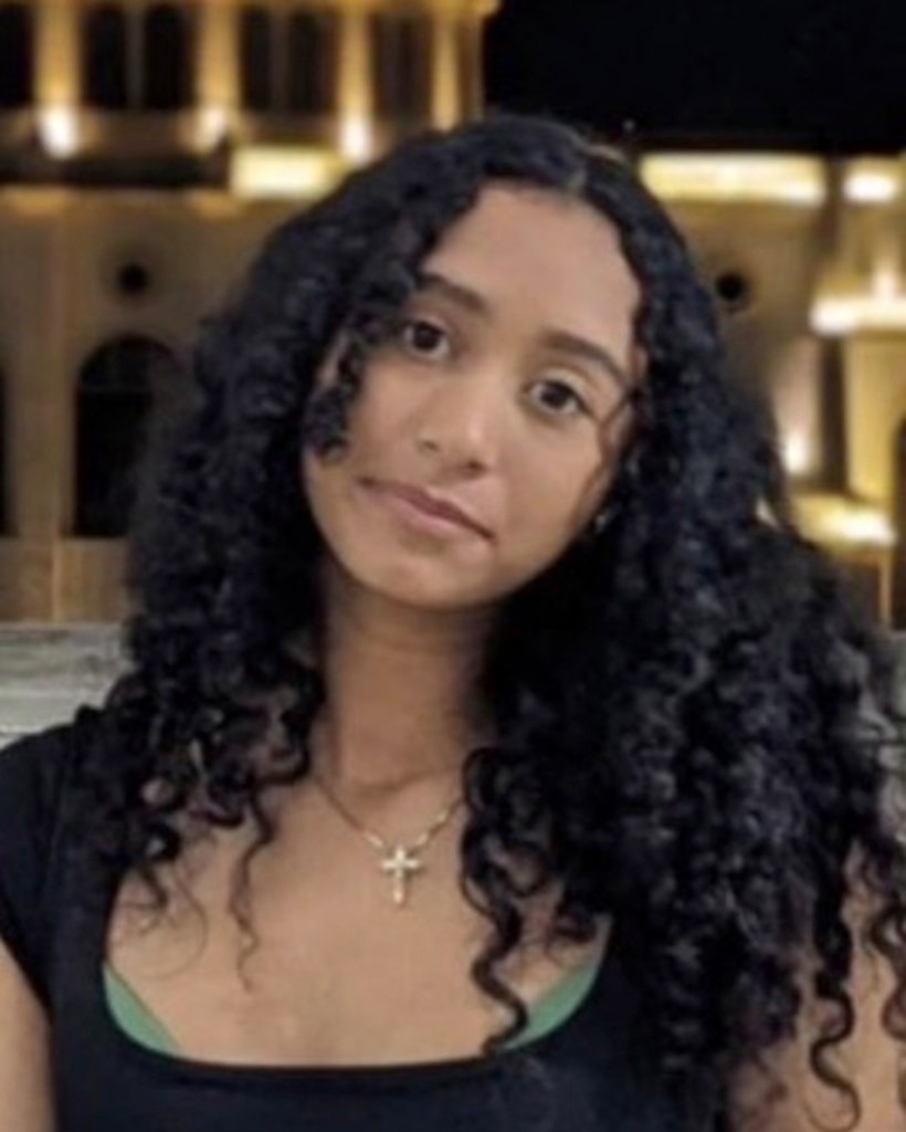 Celeste Rivas Hernandez with long curly hair and a cross necklace.