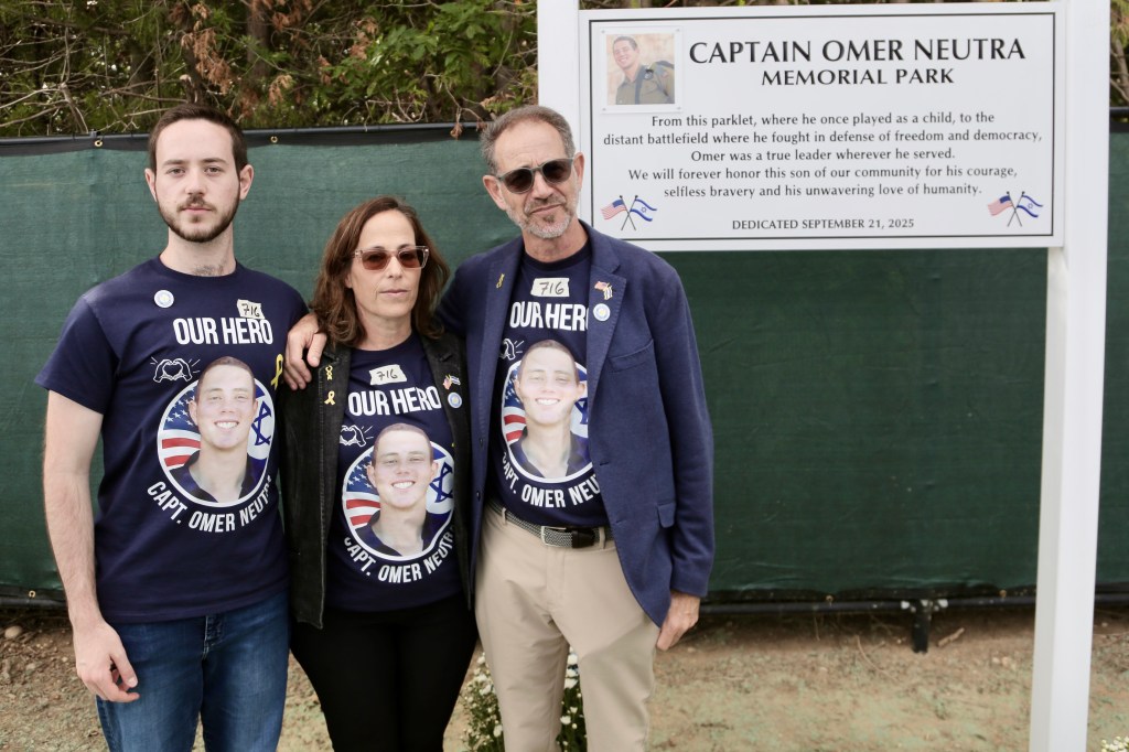 Daniel Neutra, Orna Neutra, and Ronen Neutra standing next to the Captain Omer Neutra Memorial Park sign.