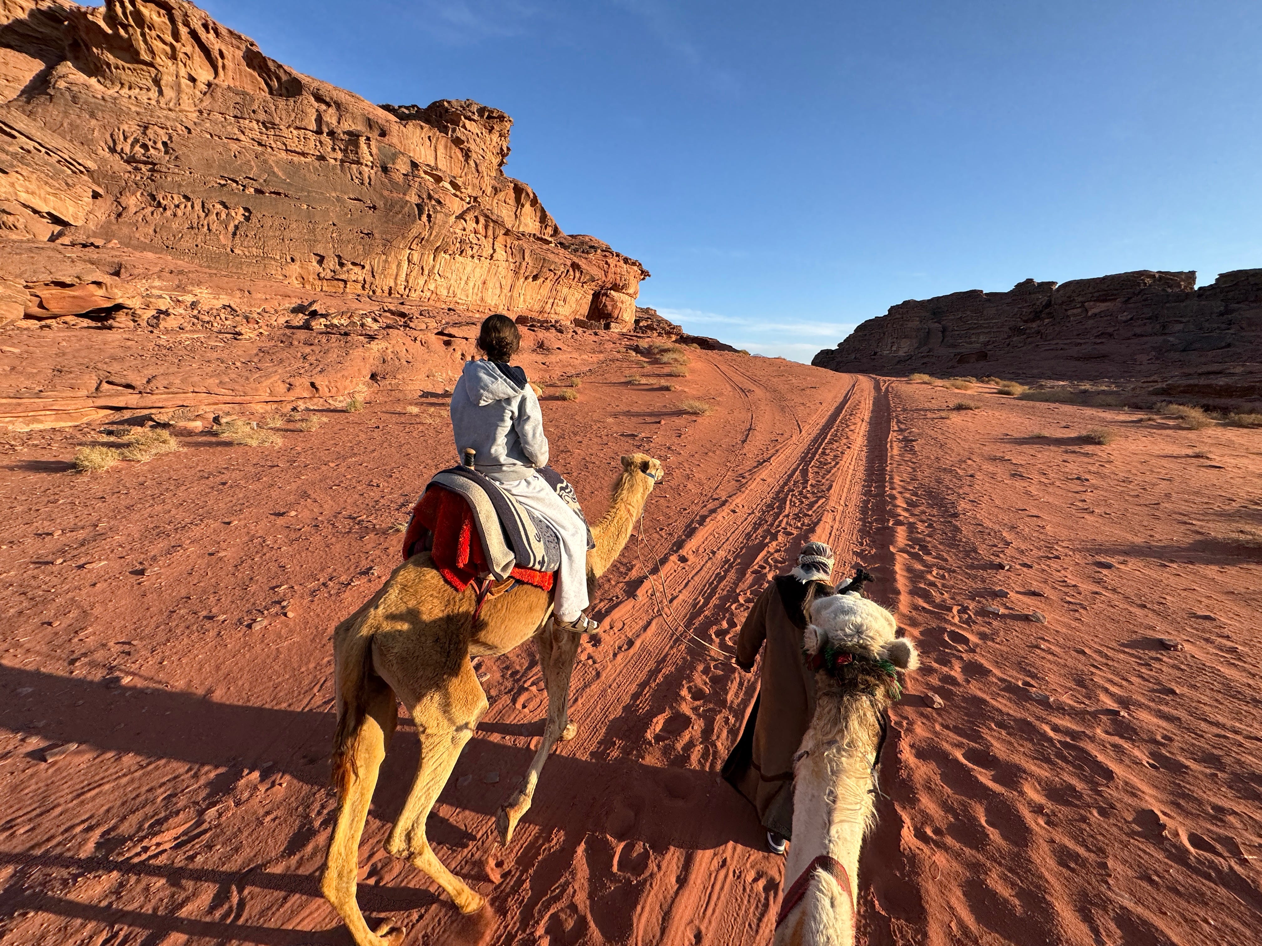 A teen is riding atop a camel being led by a guide in Jordan.