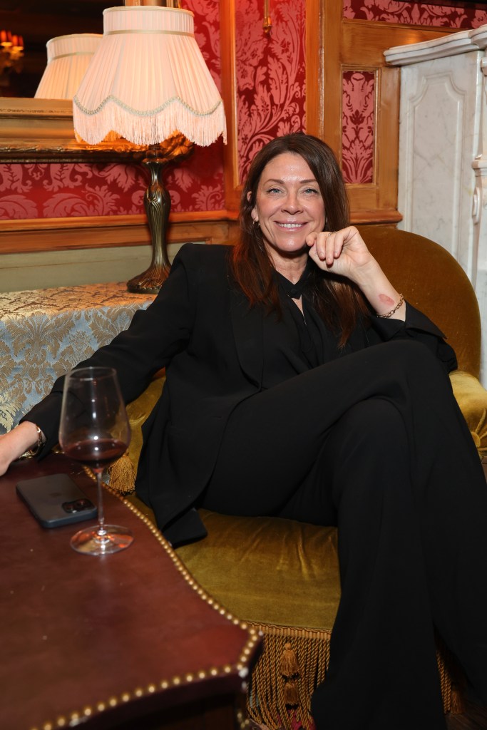 Jessica Reed Kraus sits on a couch in a black pantsuit.