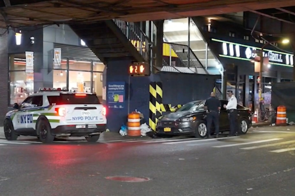 An NYPD police car and officers investigating a scene on a street at night.