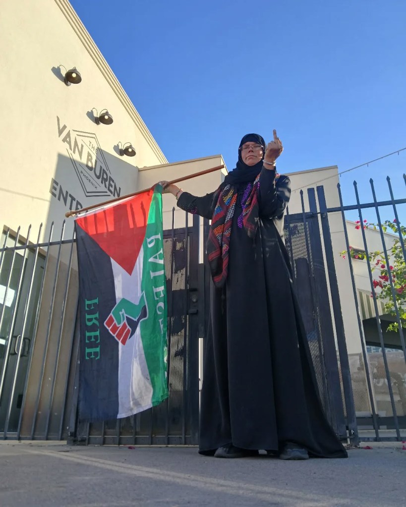 A woman holding a Palestinian flag and giving the middle finger in front of The Van Buren building.