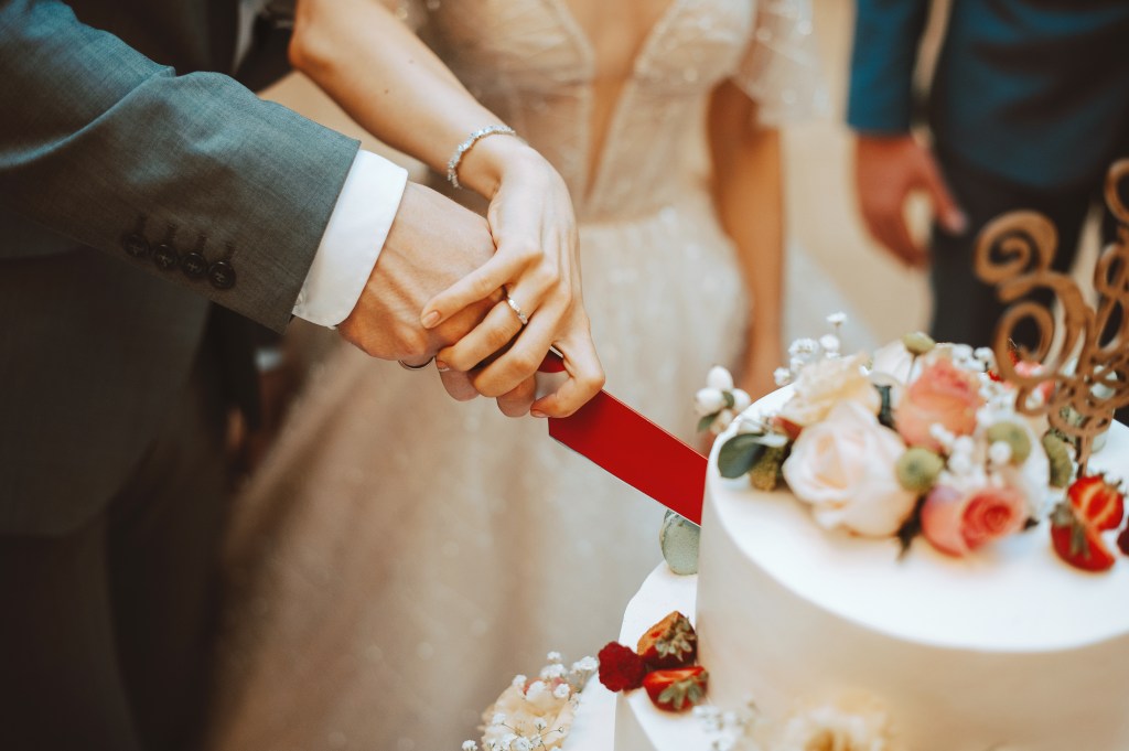 Happy couple, a bride and groom, cutting a wedding cake.