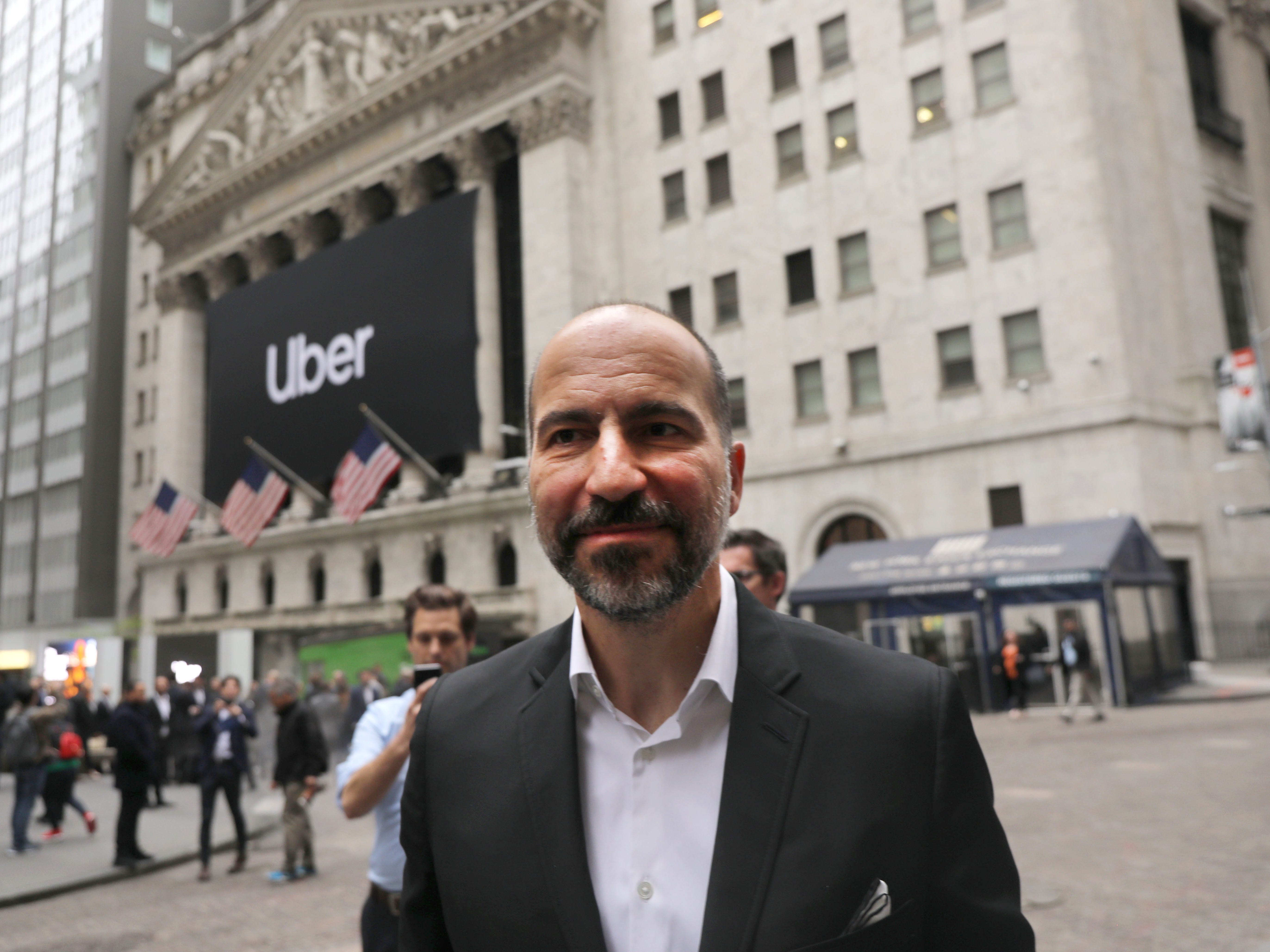 Uber CEO Dara Khosrowshahi wearing a suit on a city street with an Uber billboard in the background.