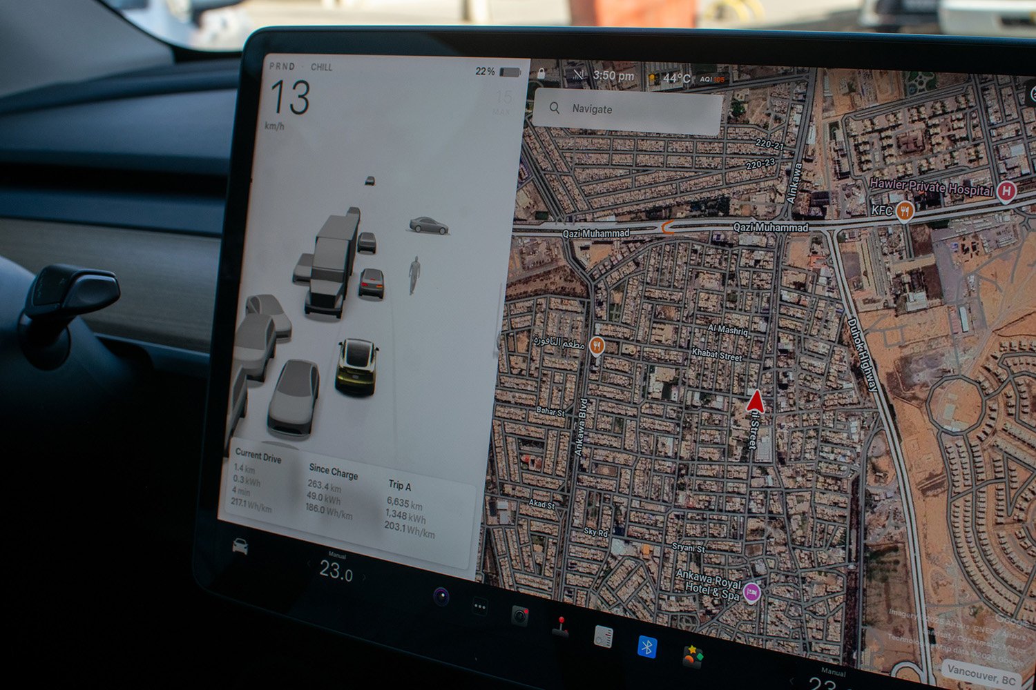 A large screen inside a Tesla car shows a street view of Erbil.