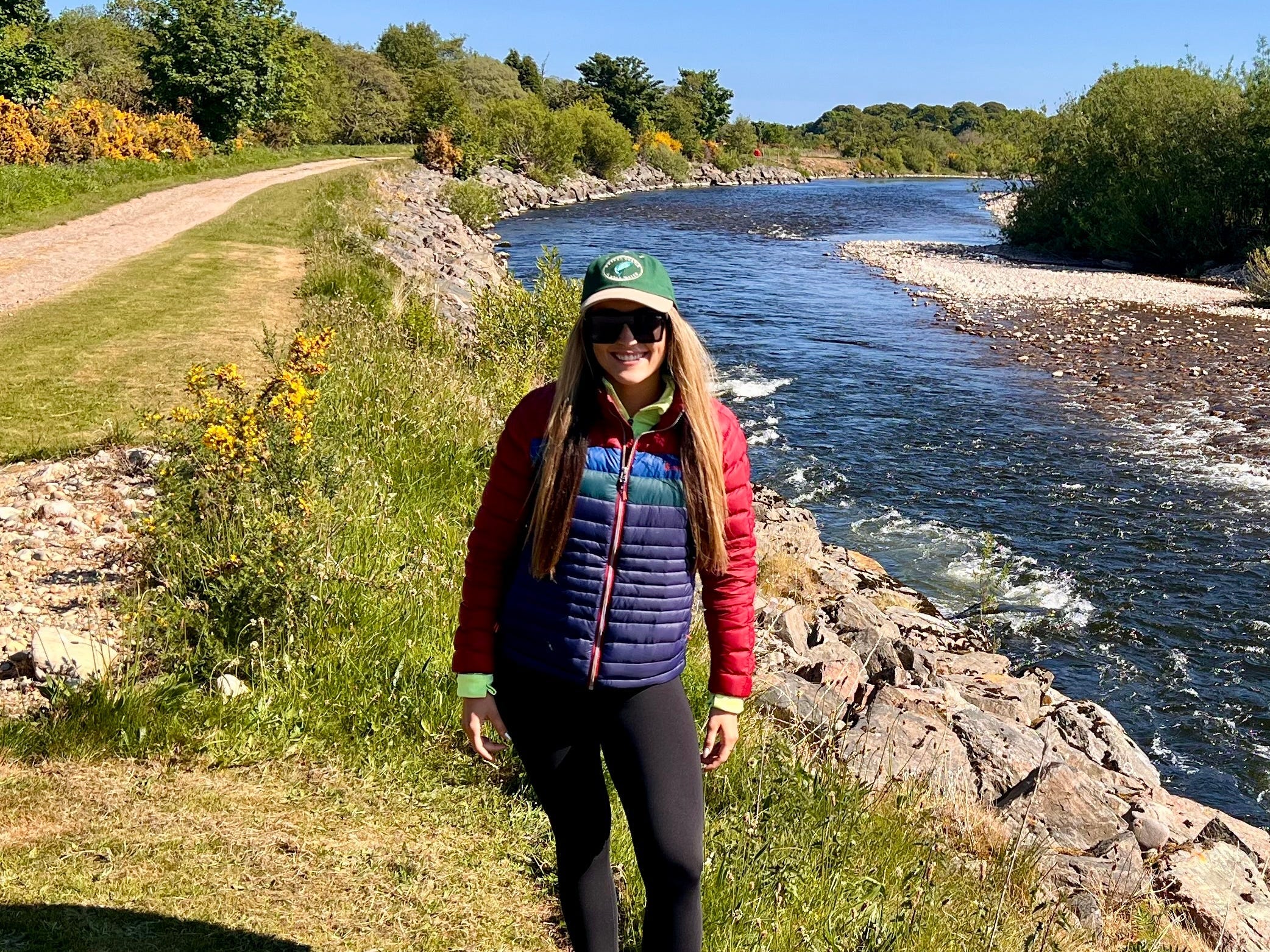 Gentry standing on the River Spey, wearing leggings, a puffy coat, and a green hat.