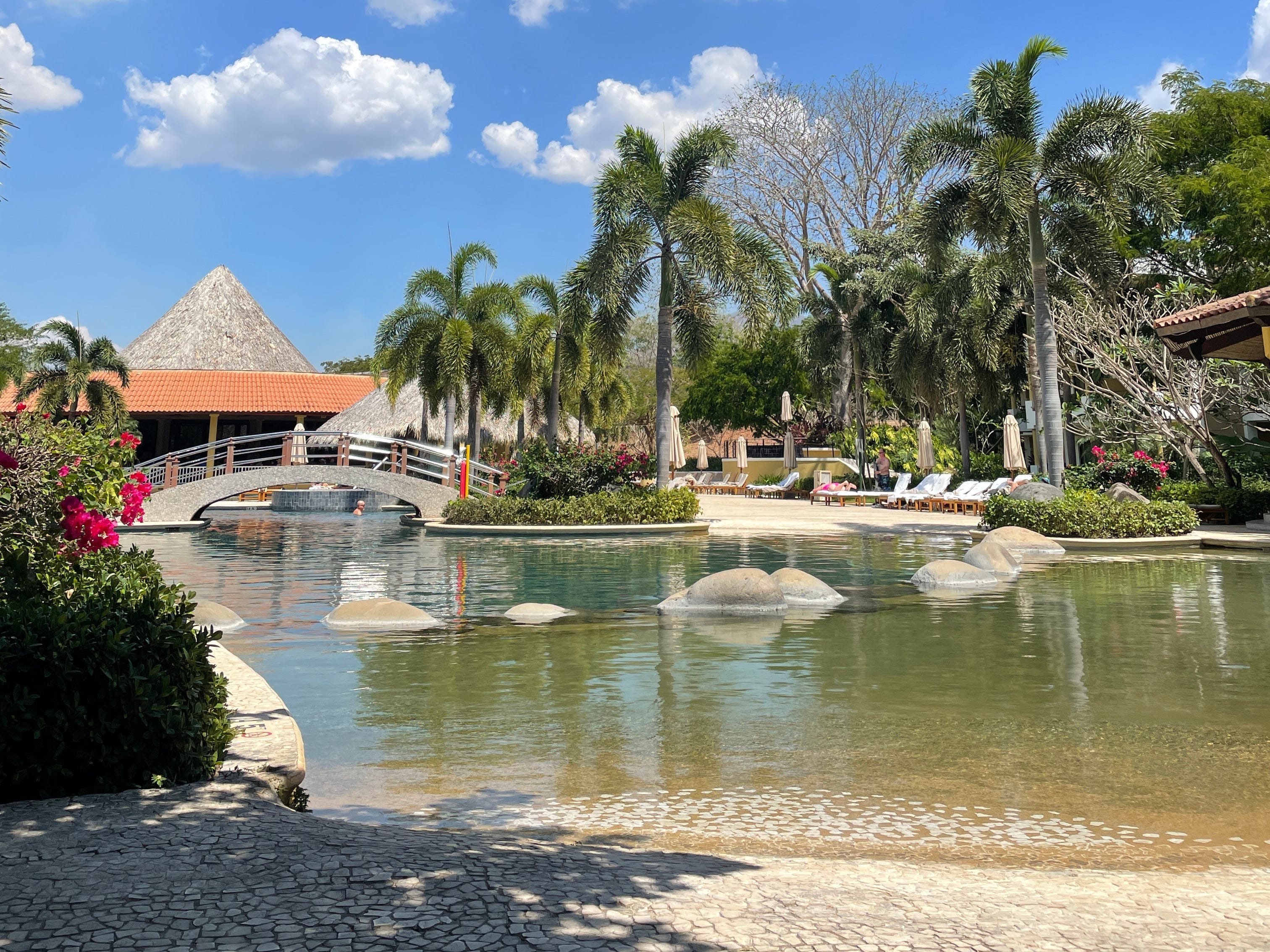 A resort with a bridge going over a pond and palm trees.