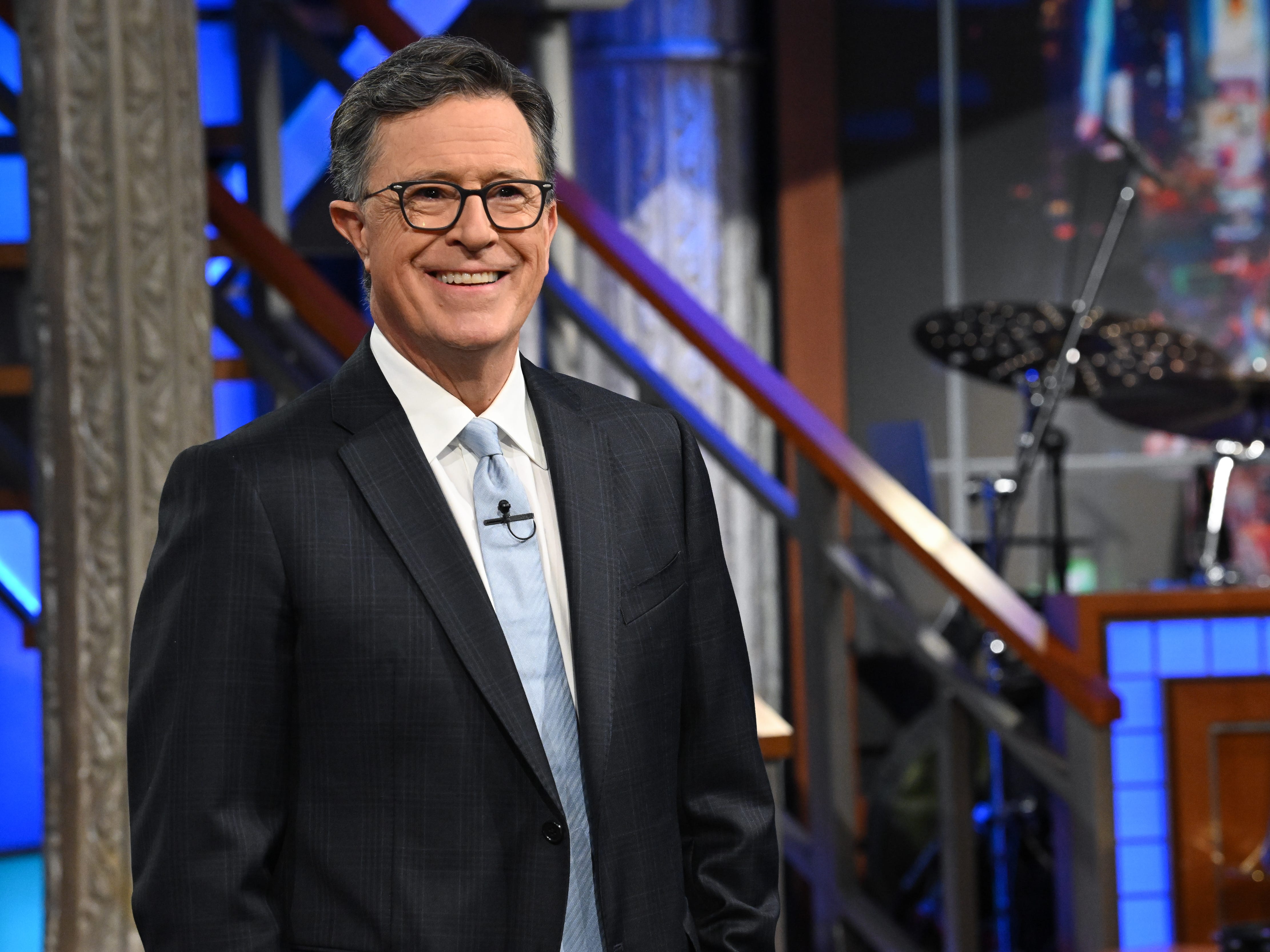 Stephen Colbert is smiling and looking ahead while wearing a suit.