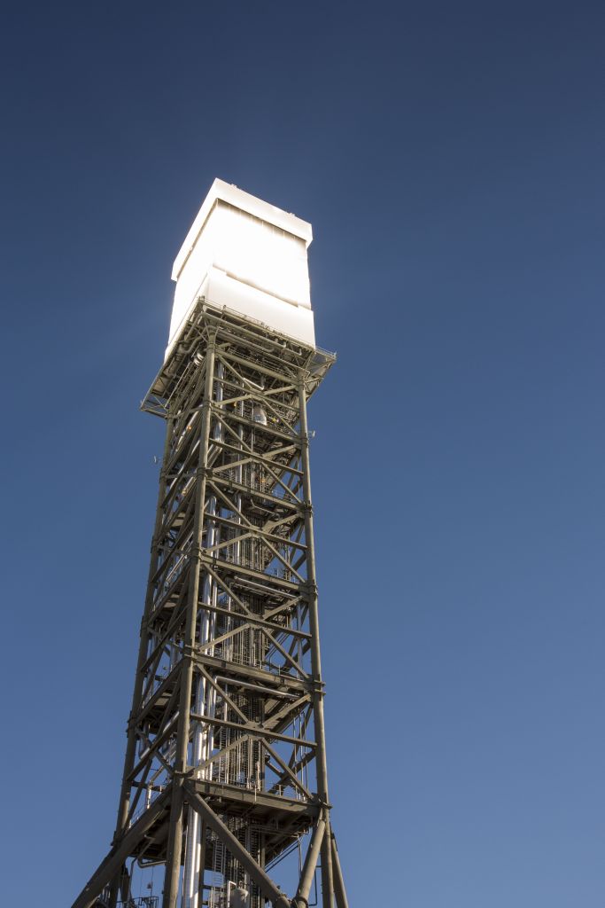Solar thermal power tower with a bright white top against a clear blue sky.