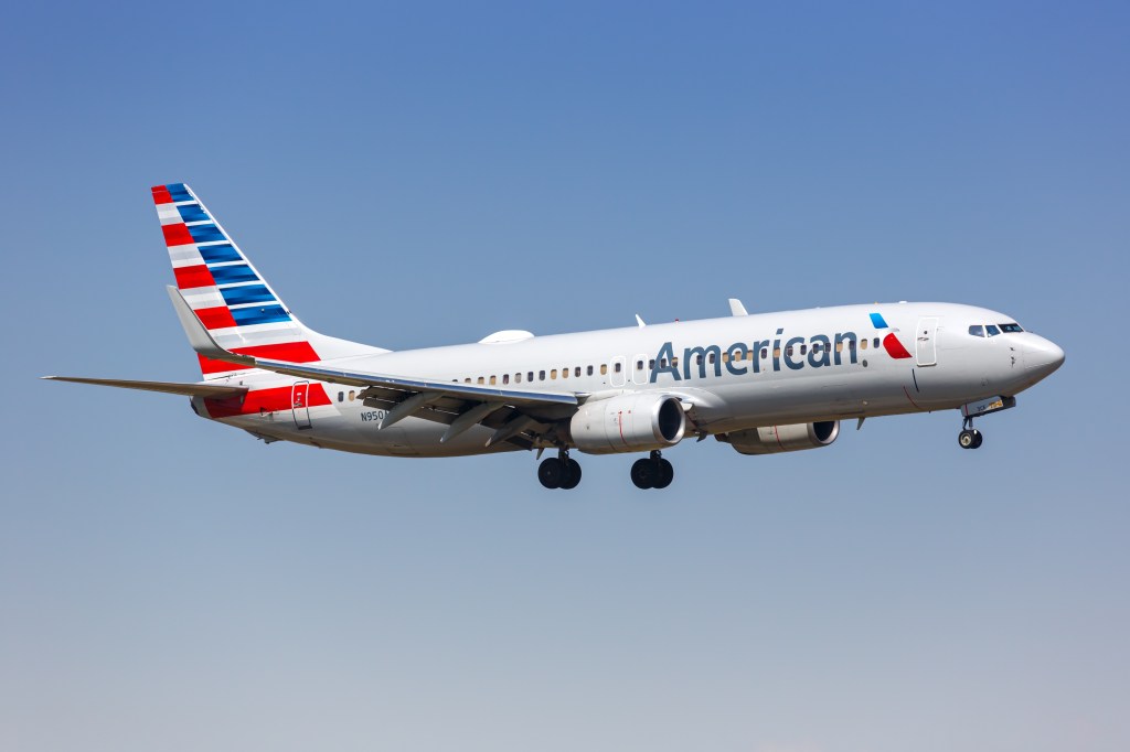 An American Airlines plane in flight against a clear blue sky.