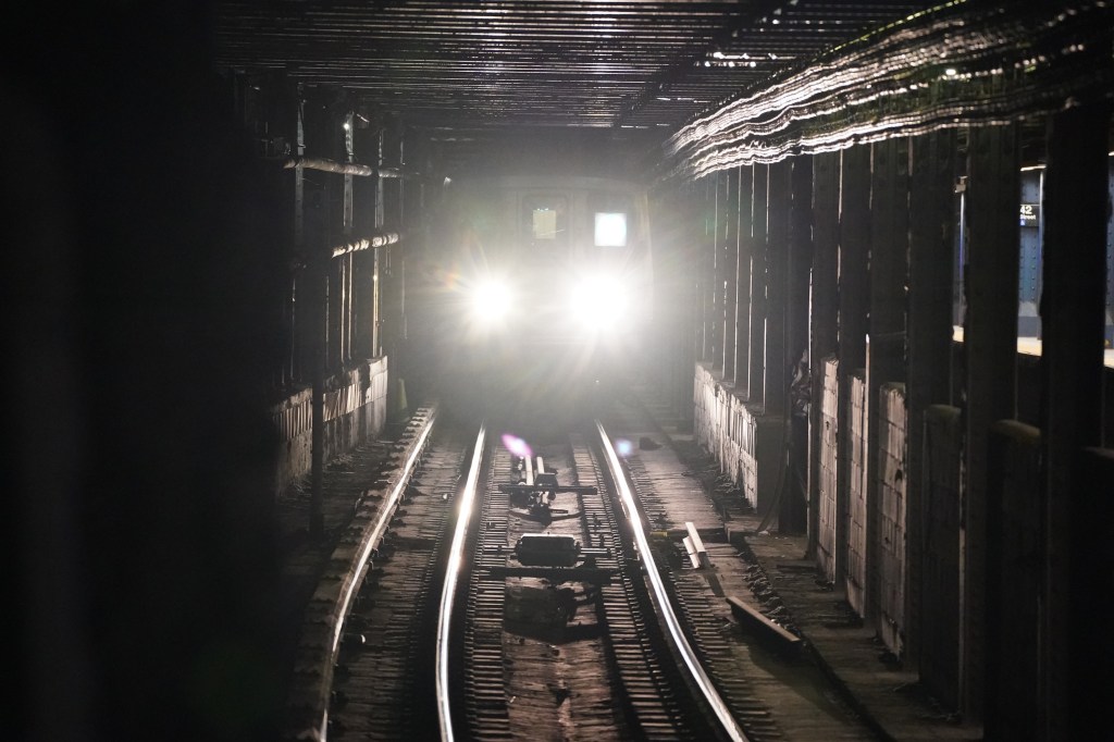 Subway train approaching with bright headlights in a dark tunnel.