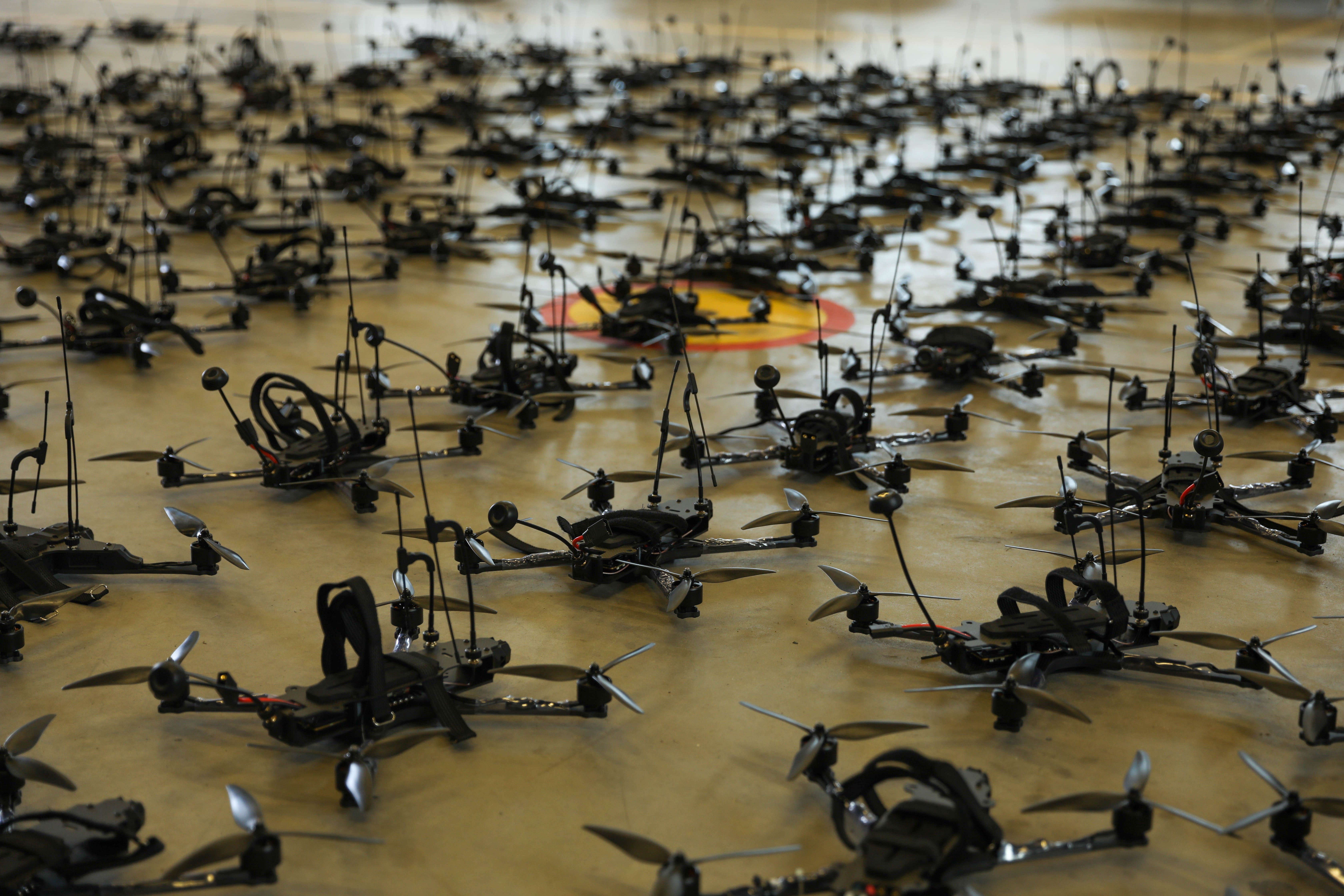 Rows of small black quadcopter drones are seen on a floor.
