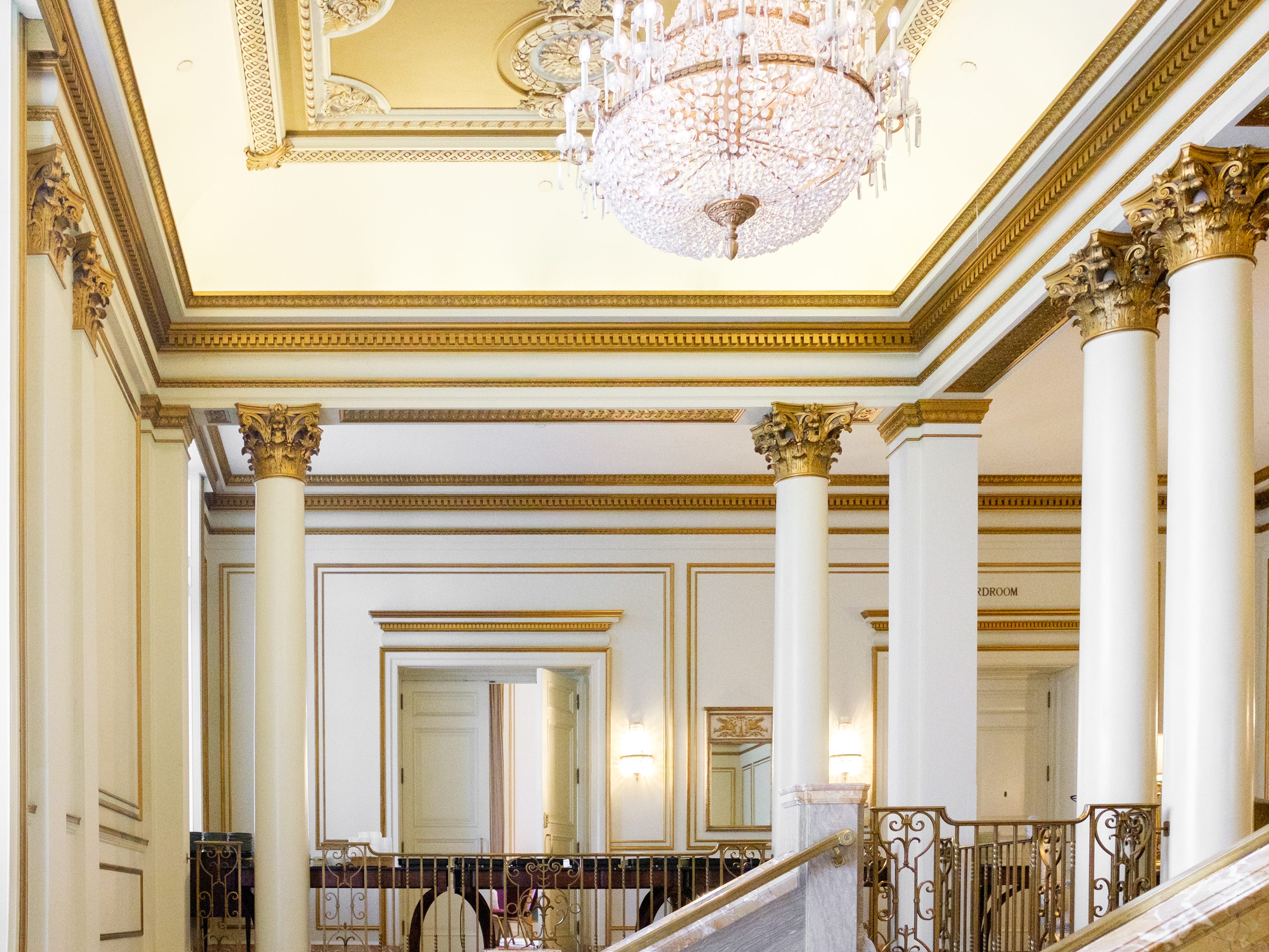A staircase with a chandelier above it leads to boardrooms with white walls and gold trimmings