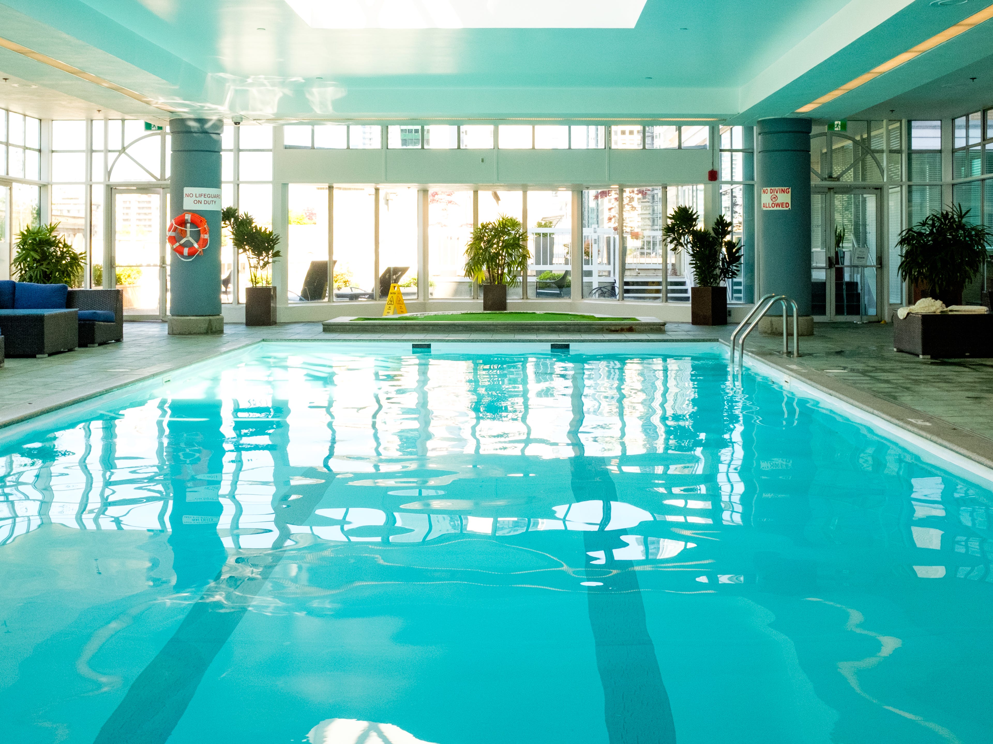 An empty hotel pool with floor-to-ceiling windows in the background and a skylight above