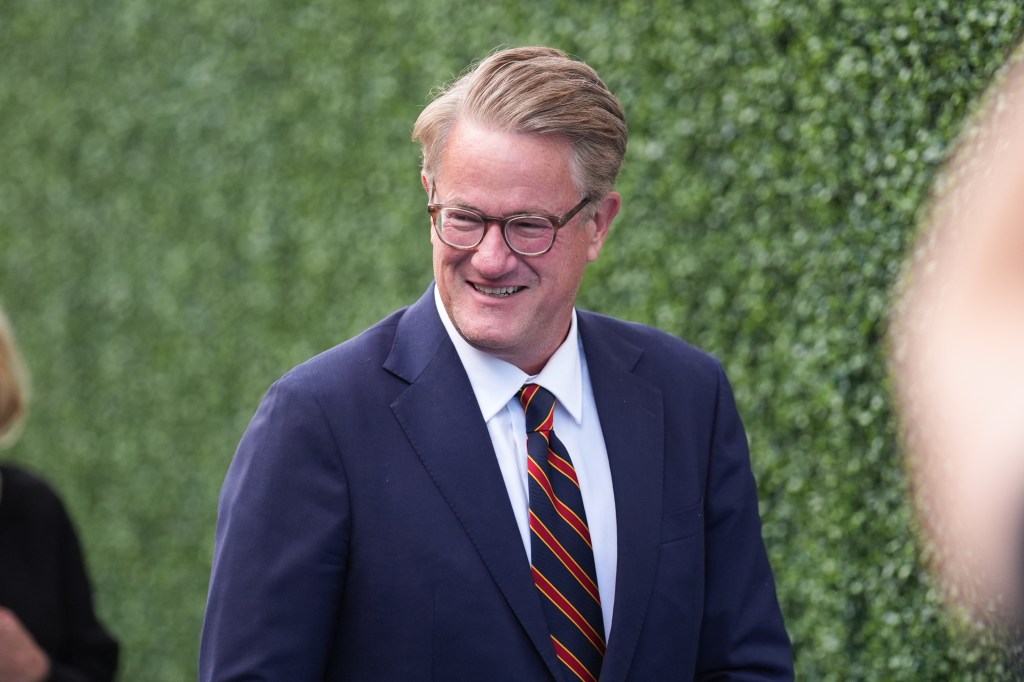 US Open attendee smiles while wearing glasses, a white shirt, a navy suit jacket, and a striped red, yellow, and navy tie.