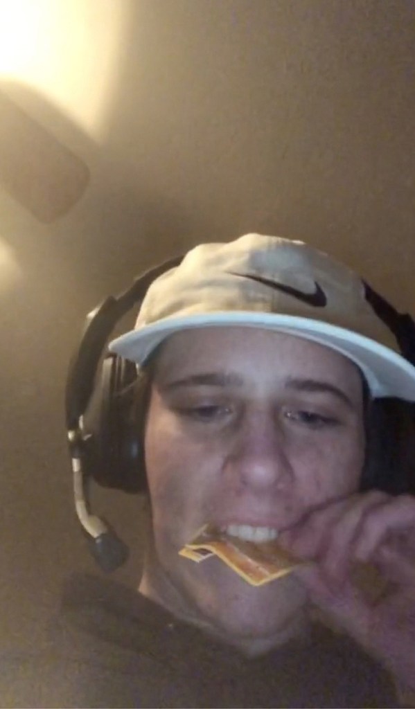 Lance Twiggs with a card in his mouth, wearing a hat and headset.