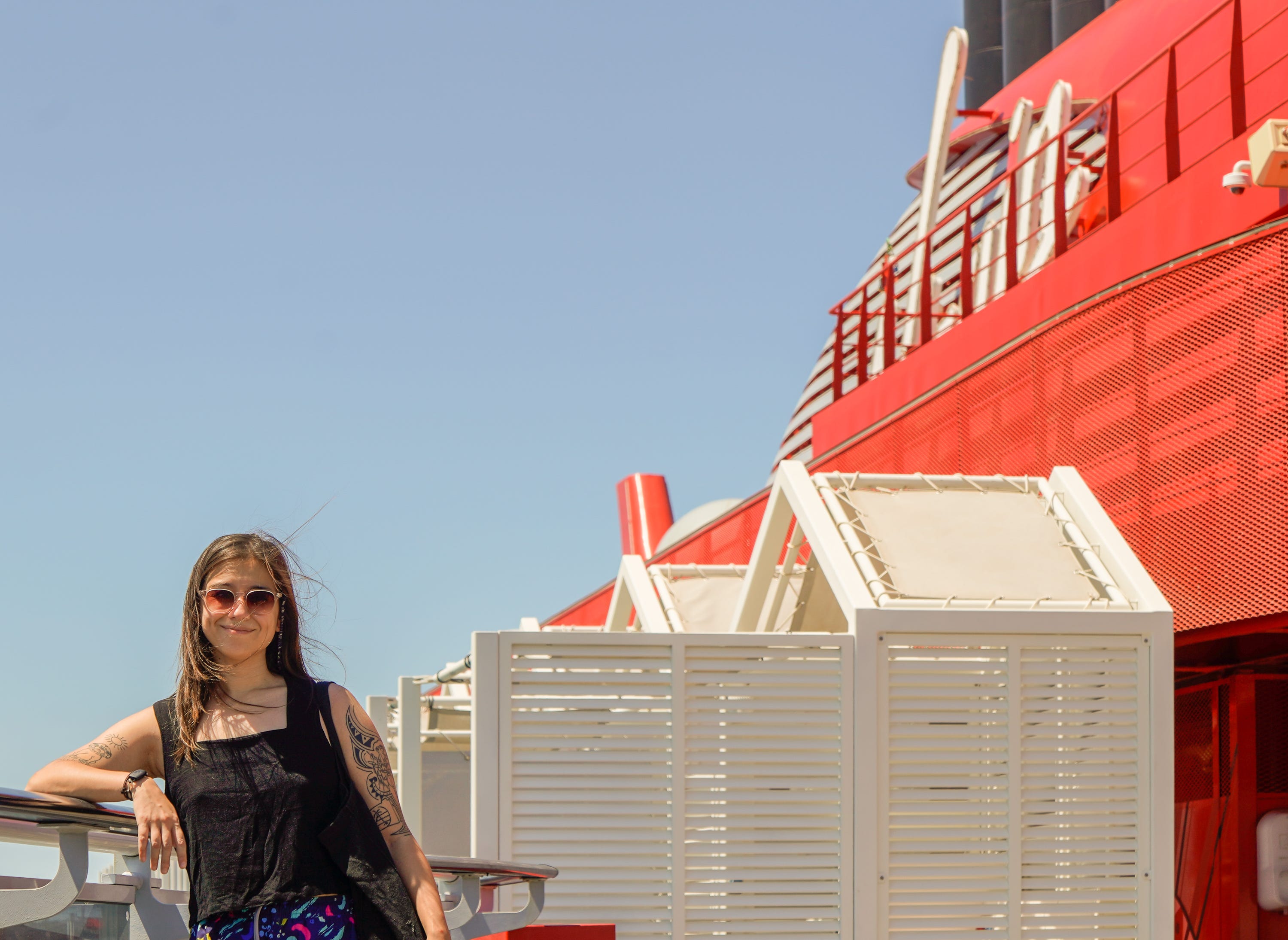 The author leans against the side of a cruise ship with blue skies behind her.