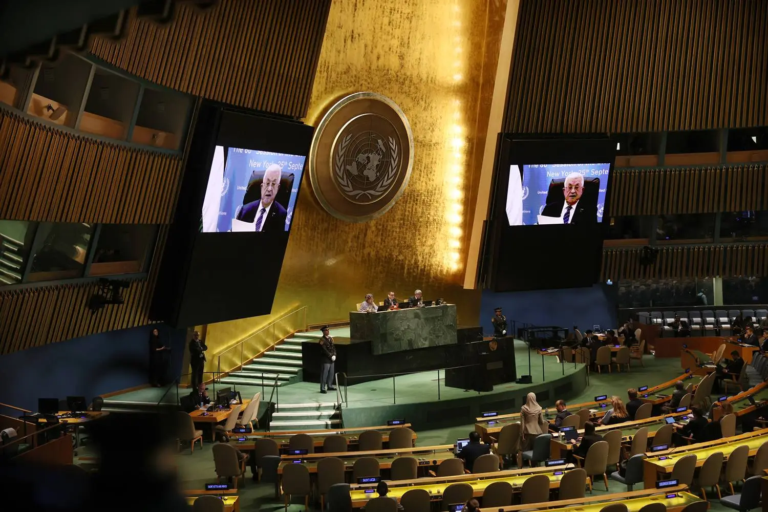 A virtual address from Palestinian Authority President Mahmoud Abbas to the United Nations General Assembly can be seen displayed on two large screens as people in the assembly hall look on.