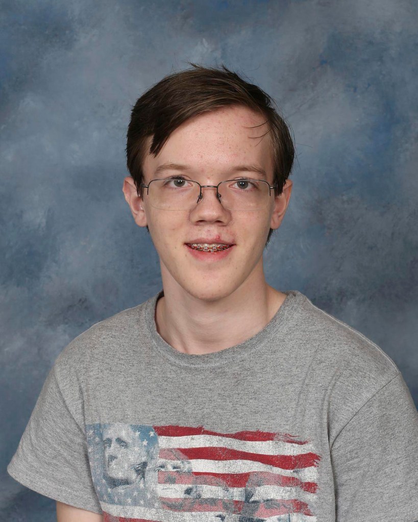 Thomas Matthew Crooks, wearing glasses and braces, in a gray t-shirt with an American flag design.