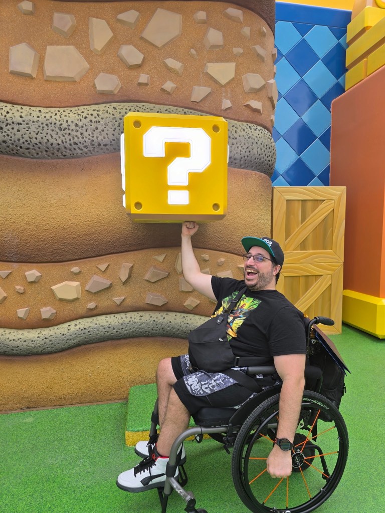 A man in a wheelchair holding up a Super Mario question mark block.