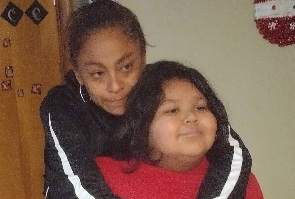 A woman in a black and white jacket hugging a child in a red shirt from behind.