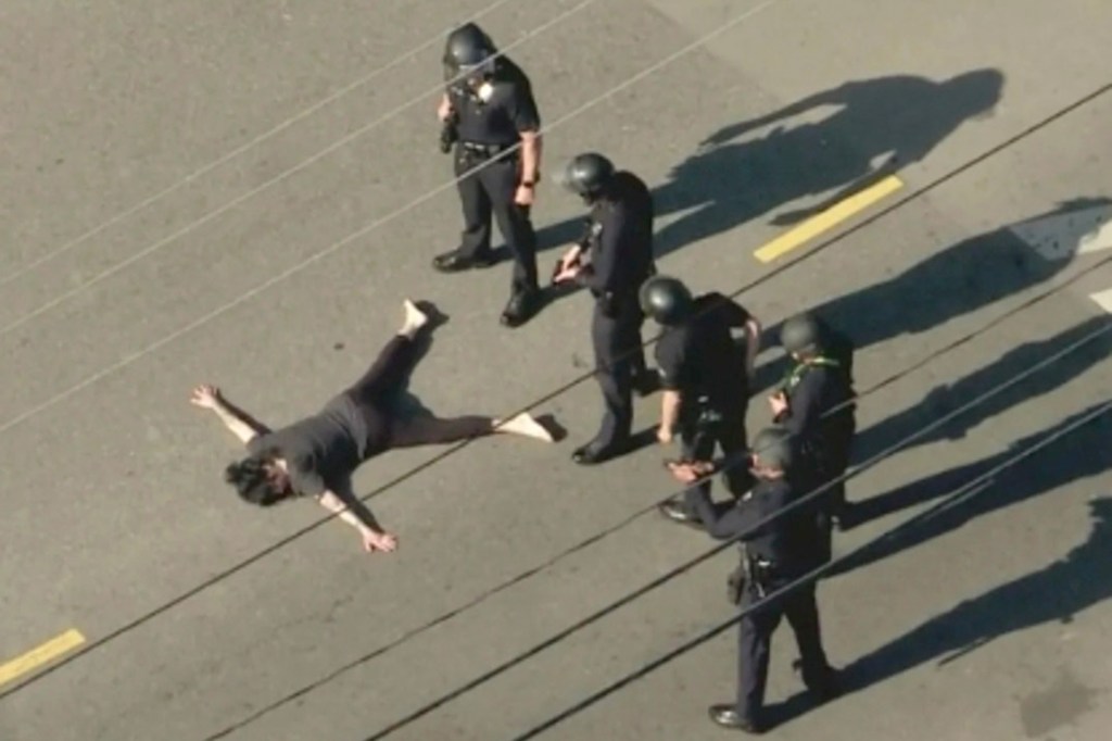 Aerial view of a woman lying on the street next to four police officers.