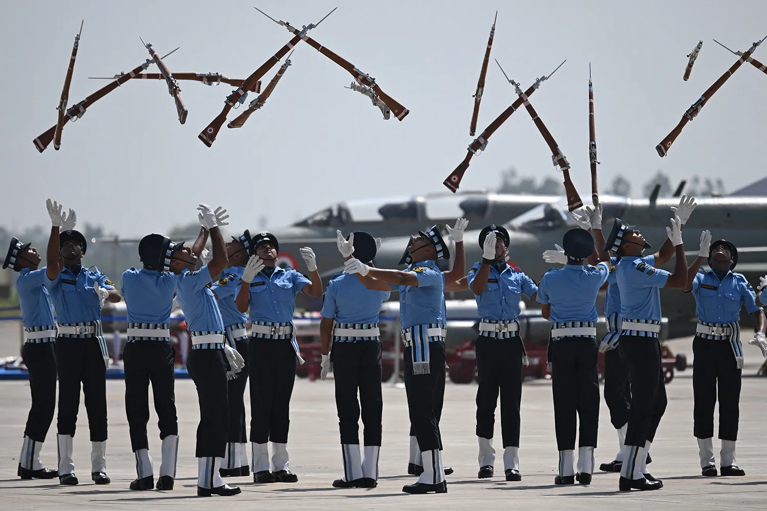 A group of cadets toss rifles in the air with white-gloved hands outstretched to catch them.