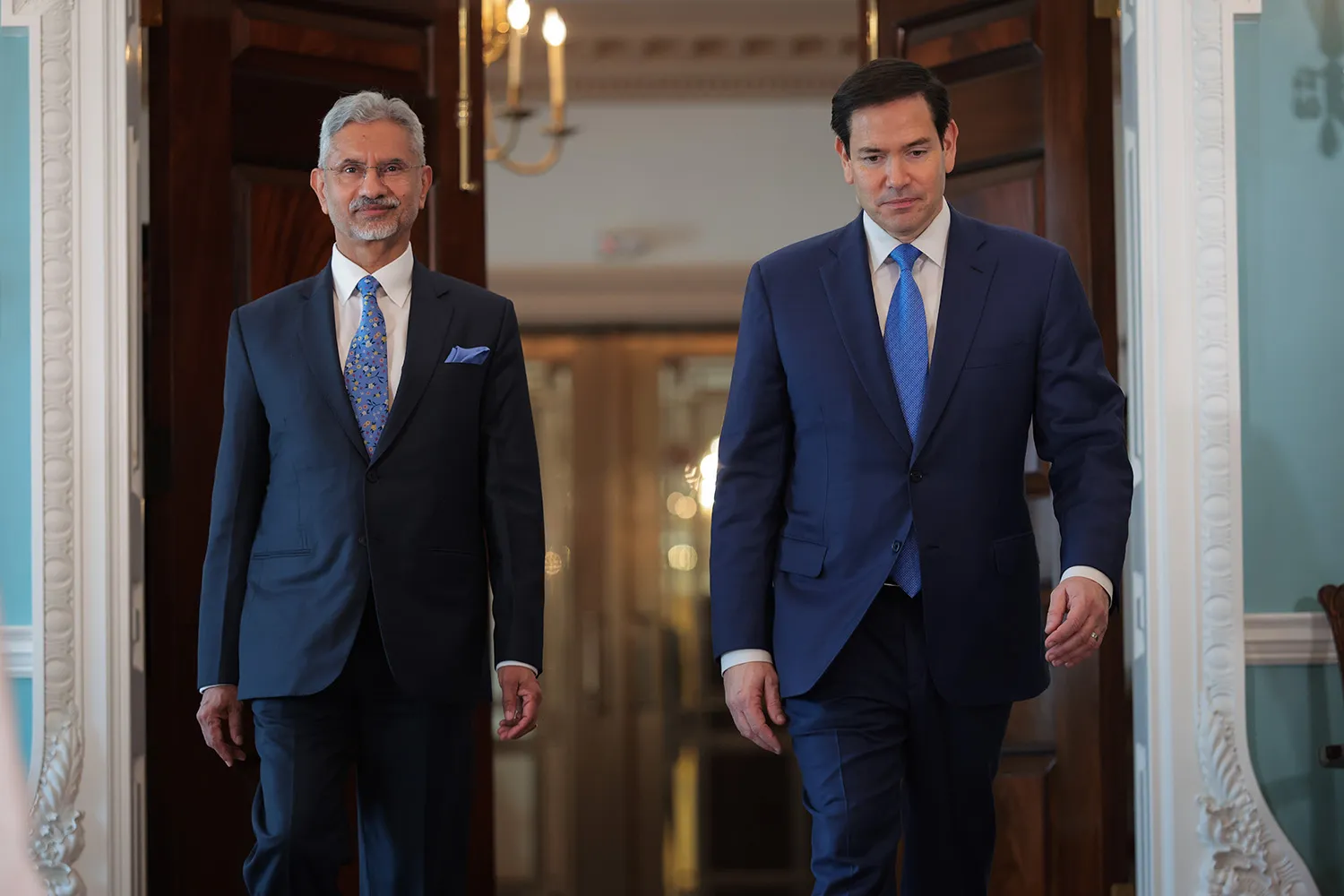 Two men in suits walk side by side through doors.