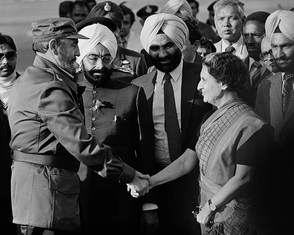 Fidel Castro and Indira Gandhi shake hands in a black and white photo.