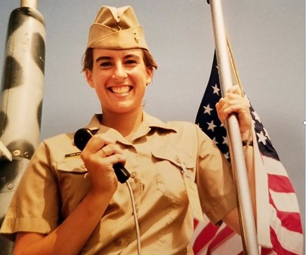 Rep. Mikie Sherrill in her Naval Academy uniform, holding a microphone and an American flag.