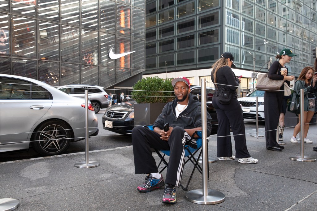 Namon Johnson, first in line at the Skims 5th Ave store, sits in a folding chair on the sidewalk in front of a Nike store.