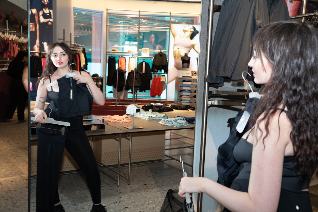 Marissa Matozzo looking at a reflection in a mirror, holding a black Nike sports top and pants.