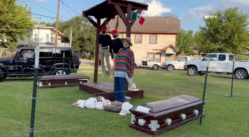 Halloween display depicting two mannequins hanging from gallows and two on the ground, with coffins and a Mexican flag.