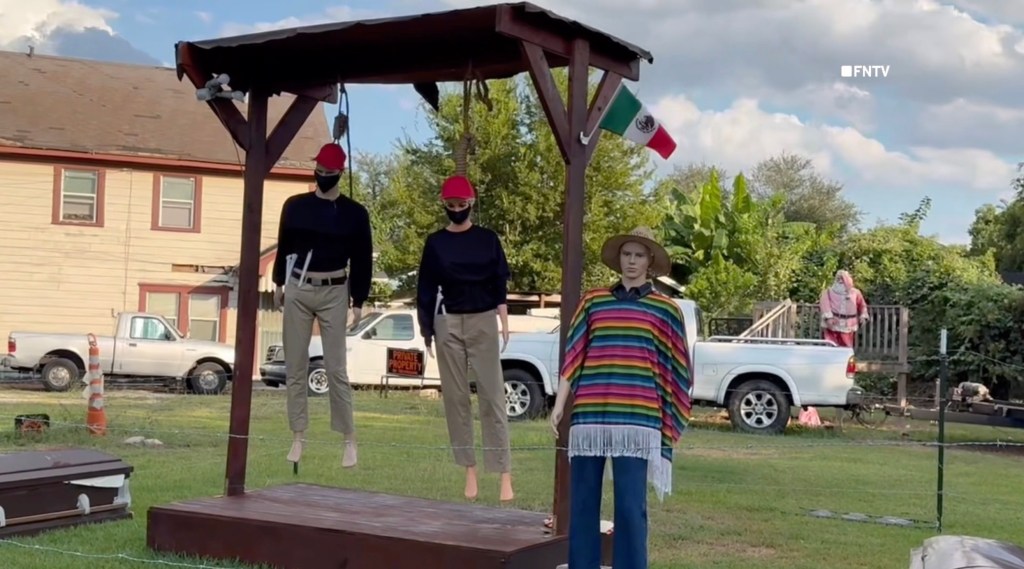 Halloween display featuring two mannequins hanging from a gallows and a third standing over a tied-up mannequin.