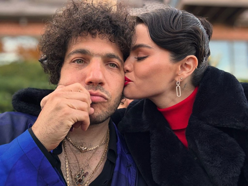 Benny Blanco in a blue jacket, Selana Gomez in a black jacket and red turtleneck.