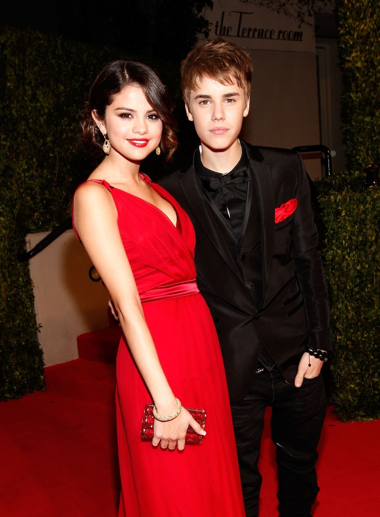 Selena Gomez in a red gown, Justin Bieber in a black suit, black shirt and tie, with red handkerchief.