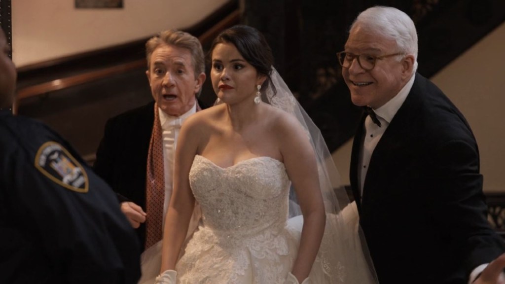 Selena Gomez in a wedding dress and veil, Martin Short in a black oat and white shirt and scarf, Steve Martin in black suit.
