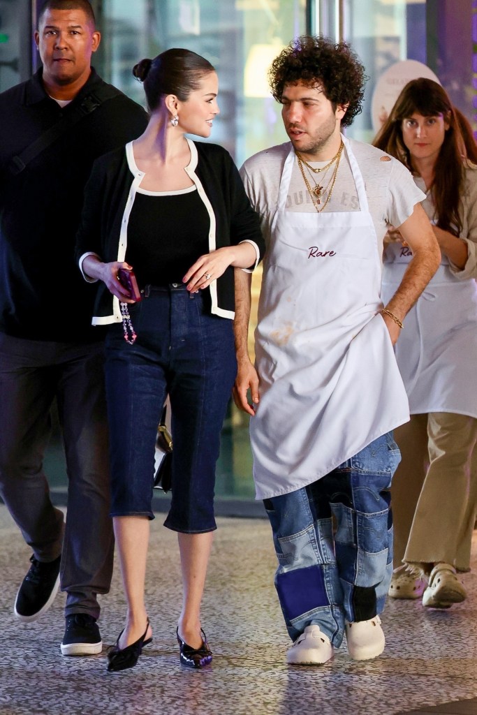 Benny Blanco in a white apron, t-shirt and jeans, Selena Gomez in a black top, black cardigan and white trim, and blue cropped jeans.