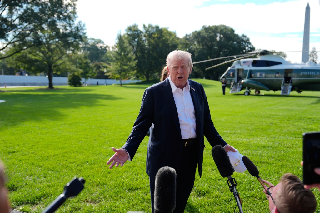 President Donald Trump speaking to reporters with a helicopter and the Washington Monument in the background.
