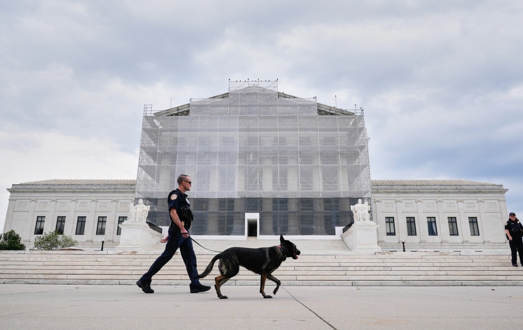 U.S. Capitol Police officer with a K9 detector dog patrolling outside of the Supreme Court, which is partially covered in scaffolding.