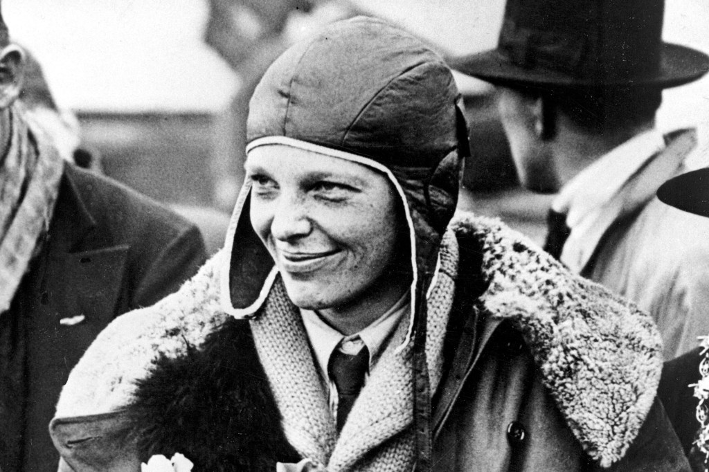 Amelia Earhart smiling while wearing a pilot's cap and a fur-collared jacket.