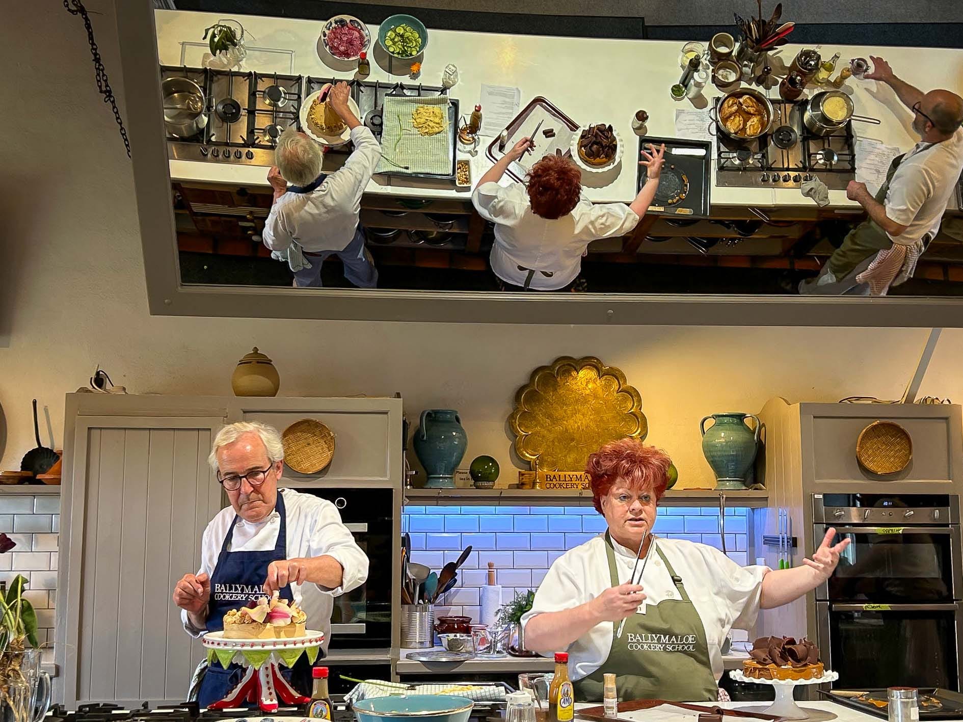 Chefs cooking in a demo kitchen, with a large tilted mirror above them.