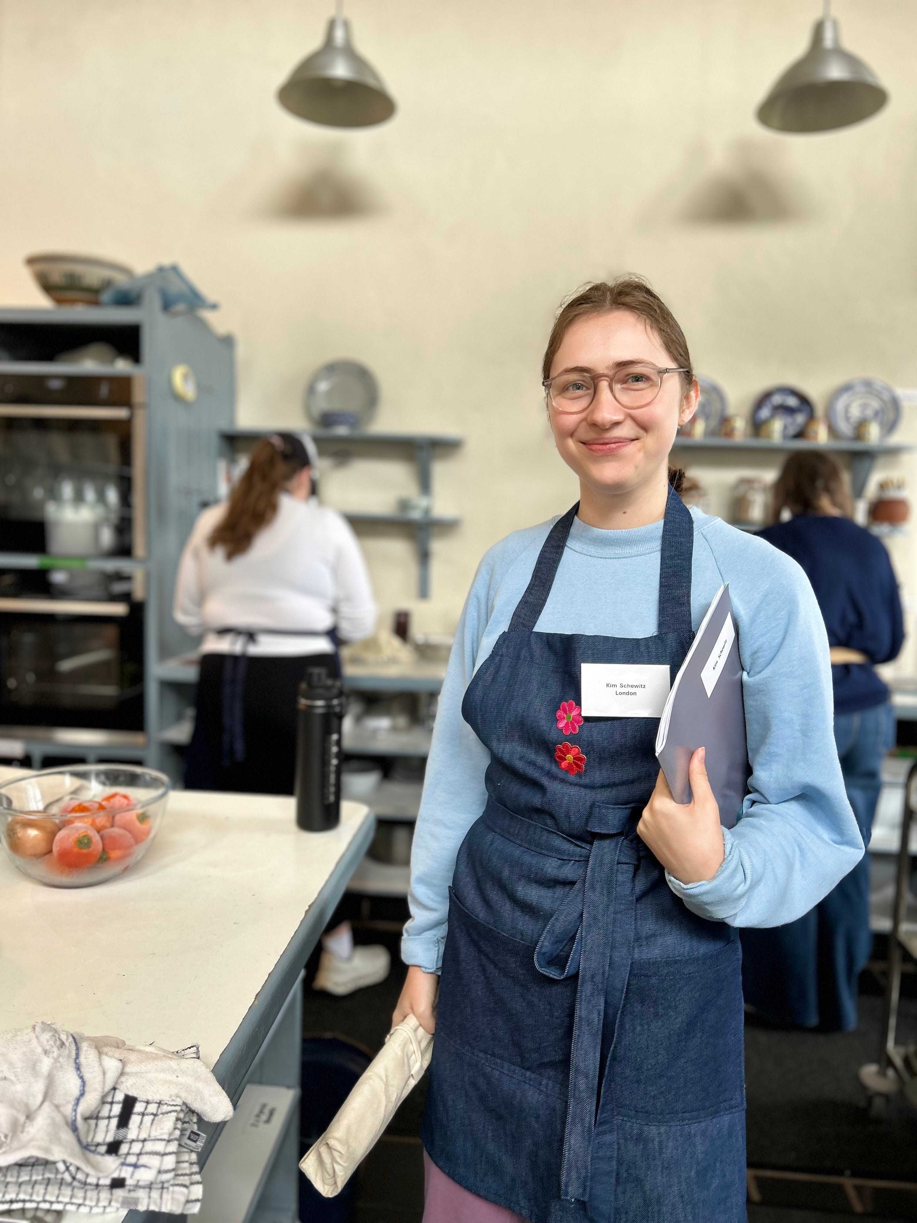 A woman smiling and wearing an apron in a large kitchen.