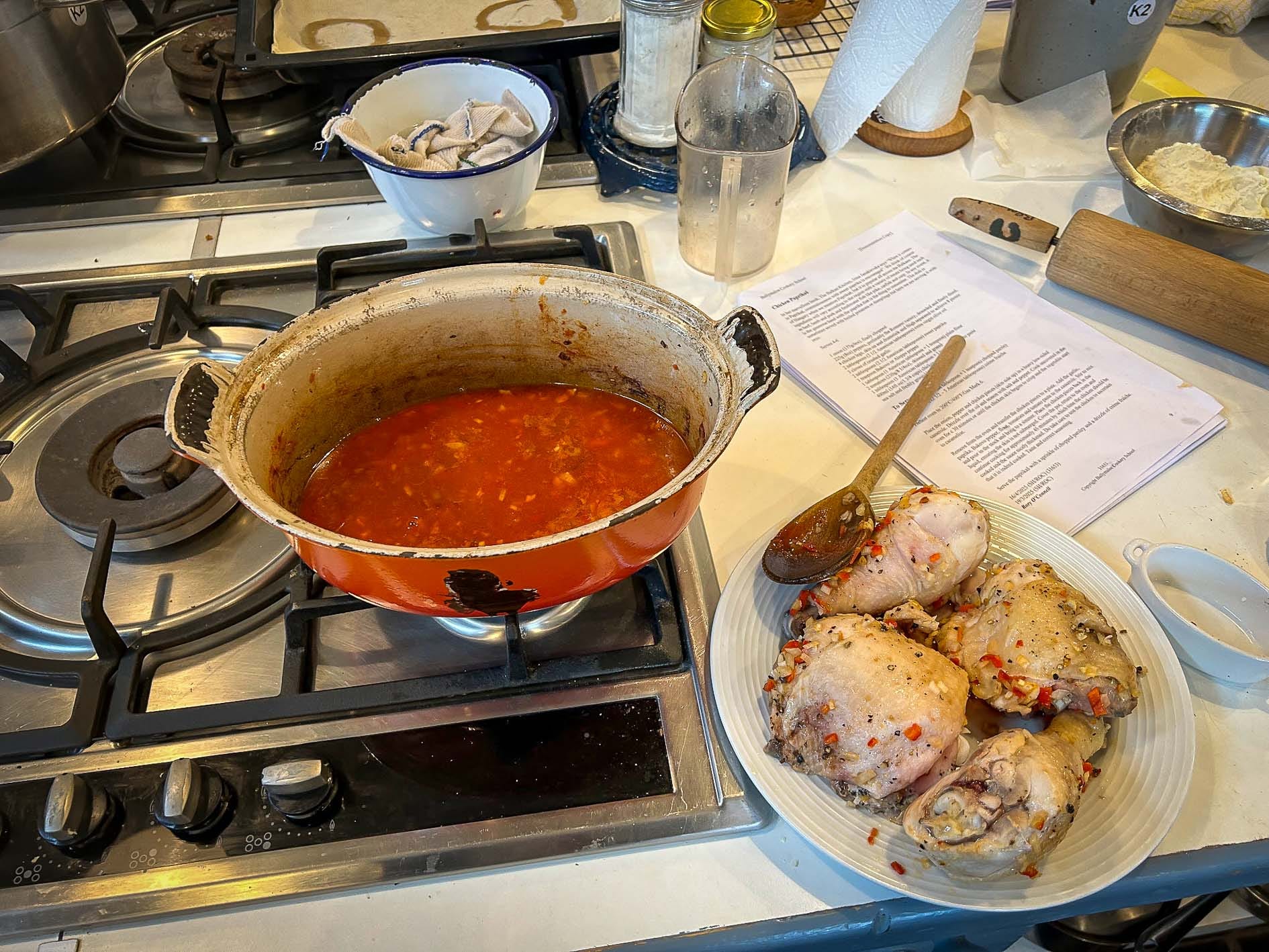 A pot of red sauce on the stove next to a plate of cooked chicken thighs covered with spices.
